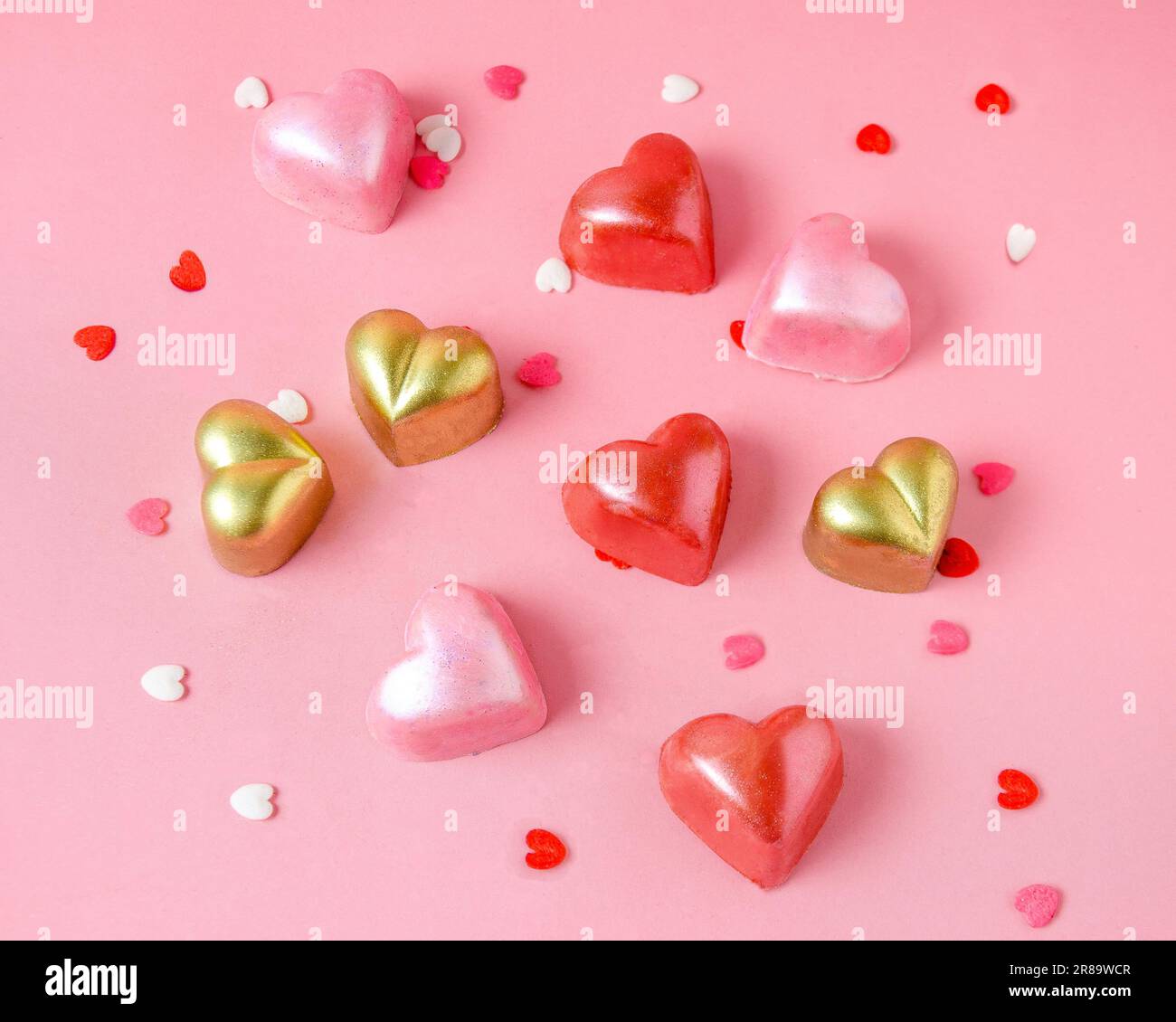 Schokoladenbonbons in Form von rosa, roten und goldenen Herzen. Pinkfarbener, einfarbiger Stockfoto