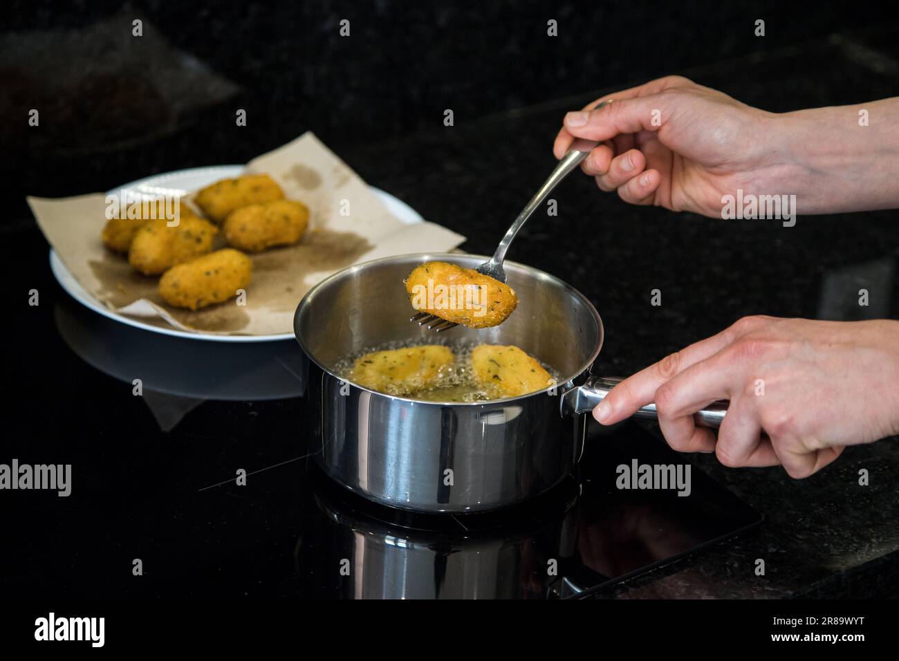 Kabeljauknödel oder „Bolinhos de bacalhau“, sehr berühmt in der portugiesischen Gastronomie. Eine Person in der Küche, die Kabeljau-Fritters brät. Vorbereitungsmodus. Stockfoto
