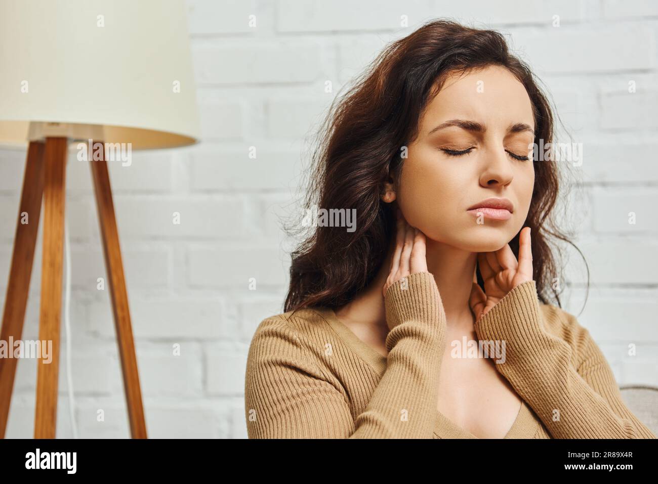 Junge brünette Frau, die die Augen während der Selbstmassage des Lymphsystems und der Schilddrüsenfunktionsunterstützung zu Hause, beim Selbstpflegeritual und bei der ganzheitlichen We schließt Stockfoto