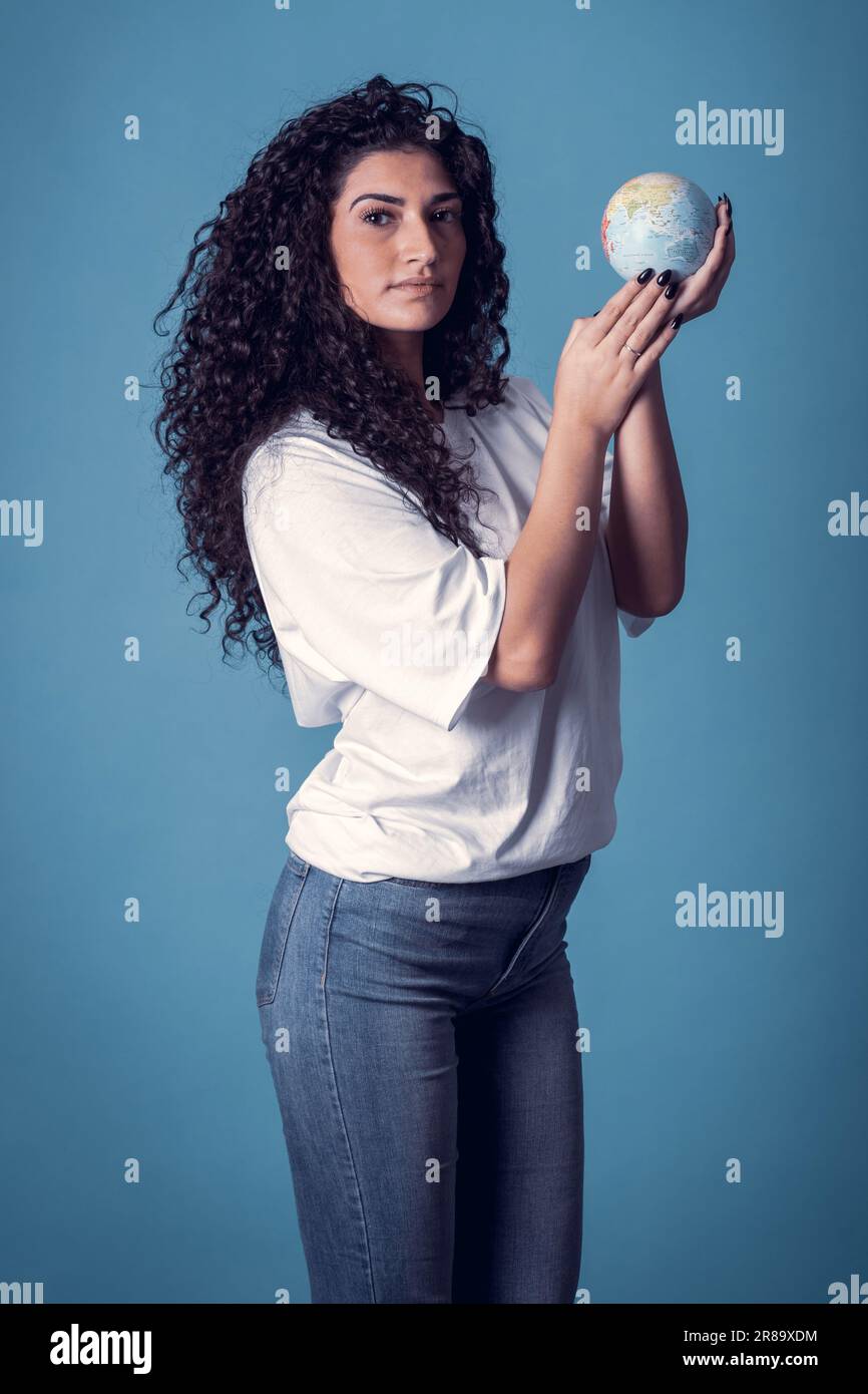 Studioaufnahme einer schönen, selbstbewussten, weißen, geschwungenen Modelin trägt blaue Jeans und ein legeres, einfarbiges weißes T-Shirt, isoliert auf blauem Hintergrund. P Stockfoto