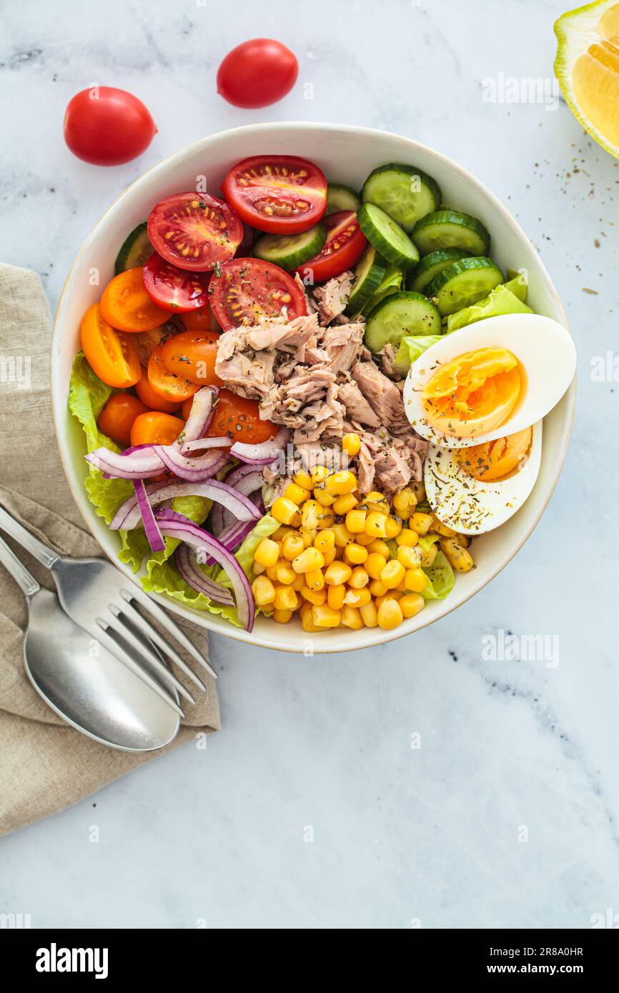 Thunfischsalat mit Ei, Gemüse und Mais in einer weißen Schüssel, weißer Hintergrund, Draufsicht. Stockfoto