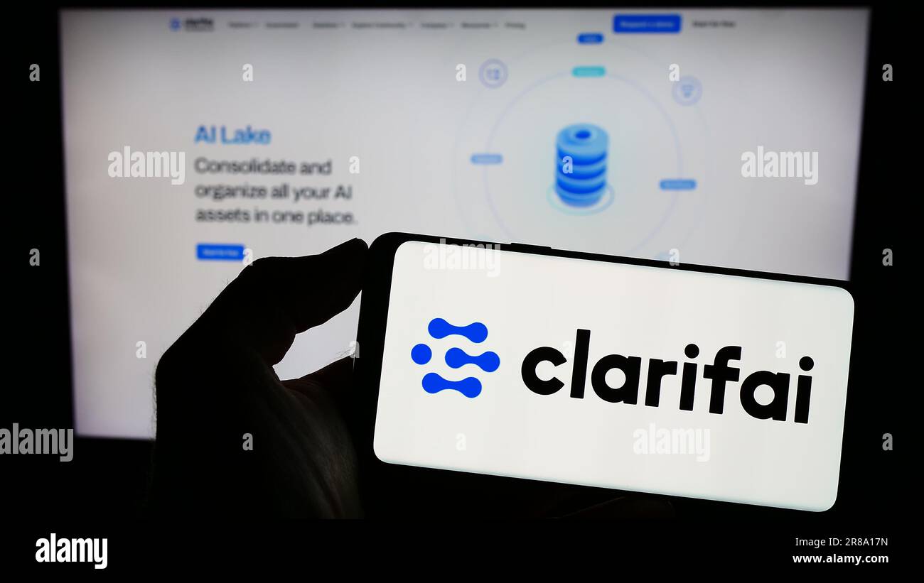Person, die ein Mobiltelefon mit dem Logo des US-amerikanischen Unternehmens Clarifai Inc. Für künstliche Intelligenz auf dem Bildschirm vor der Webseite hält. Konzentrieren Sie sich auf das Display des Telefons. Stockfoto