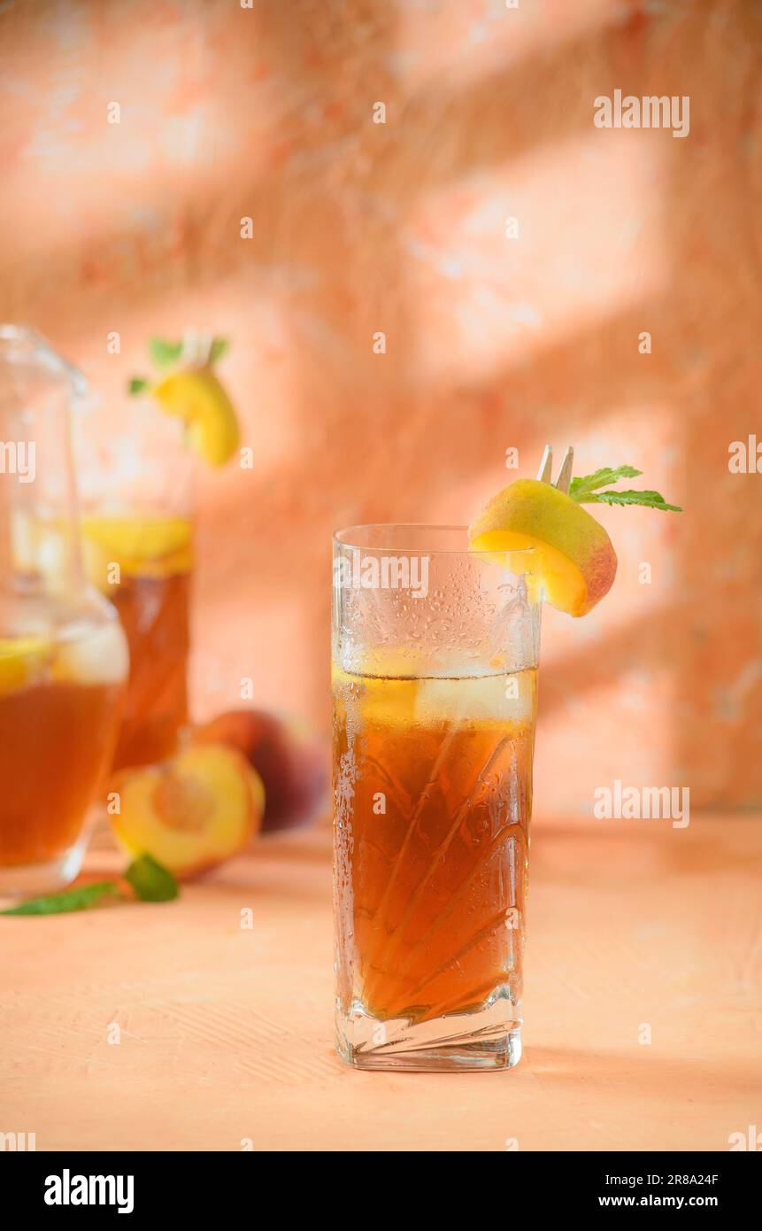 Pfirsich-Eistee-Kanne im Hintergrund. Schatten auf melonenfarbenem Hintergrund. Stockfoto