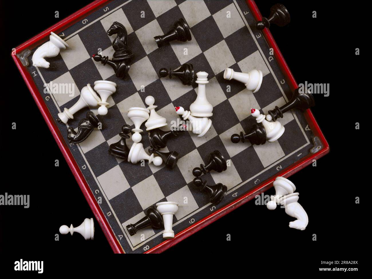 Kleine Plastikschachfiguren, die chaotisch auf einem schwarz-weißen Schachbrett liegen. Tragbares Mini-Spiel für unterwegs. Schachfiguren auf einem Brett verstreut Stockfoto