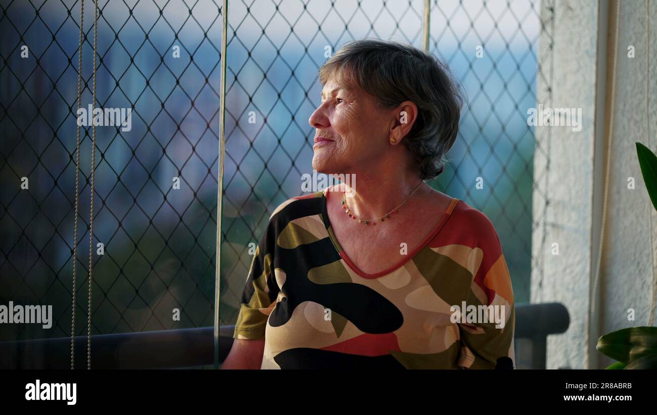 Introspektive Momente von Senior Woman's solitärer Reflexion by the Window, die sich die City View-SD zu Eigen machen Stockfoto