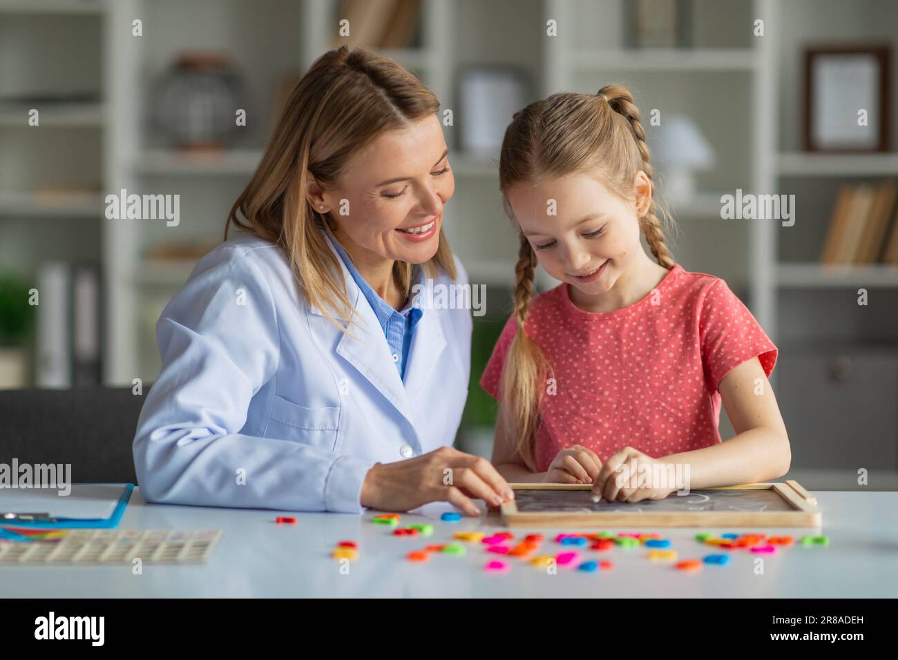 Little Girl Painting Auf Mini-Kreidetafel Während Eines Meetings Mit Einem Spezialisten Für Kinderentwicklung Stockfoto
