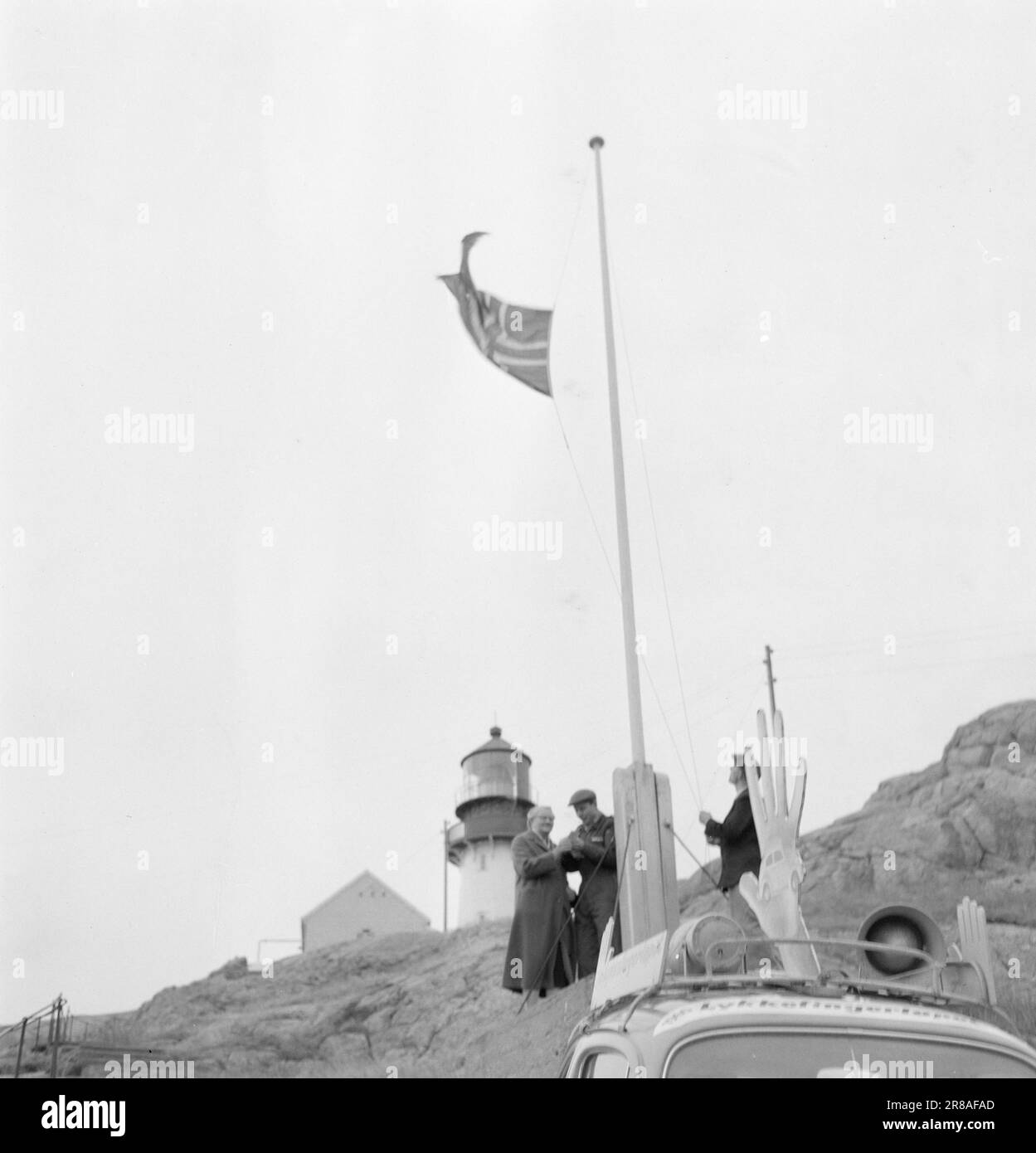 Aktuelle 48-10-1960 : Wer will ein kostenloses Auto? Das Glückswettlauf hat Lindesnes in frischen Stürmen und mit großem Erfolg umrundet. Westnorwegen und ein großer Teil des weichen Küstenstreifens sind nun mit schwarzen Reißnadeln ausgestattet. Der glückliche Fingerwagen an Norwegens Südspitze, Lindesnes. Der Leuchtturmmeister REINART Rasmussen hebt die Flagge, um die glücklichen Finger zu empfangen, während Frau Ingebjørg (links) ihrem Abgeordneten Mitarbeiter (Zentrum) ihren Fingerabdruck gibt. Vor nicht allzu langer Zeit war der öffentliche Wagen aus Lykkefinger auf der Nordkapp - der Wagen ist genauso gut gefahren wie der lykkefingerløpet. Foto: Bjørn Bjørnsen Stockfoto