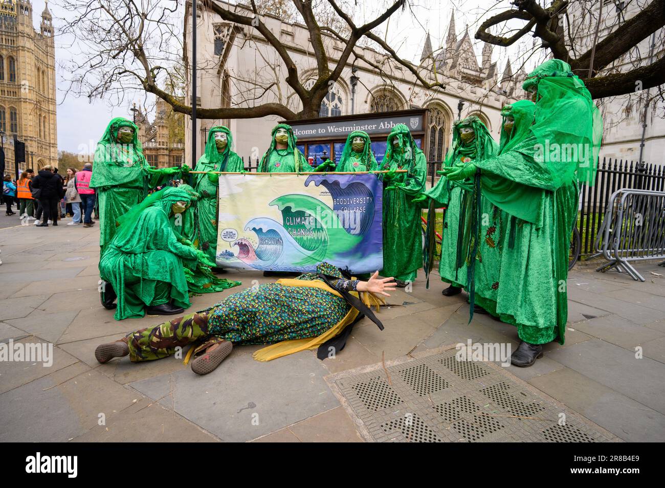 LONDON - 22. April 2023: Green Spirits bei XR march in London, posieren mit einem Protestbanner vor Westminster Abbey und Houses of Parliament in Parli Stockfoto