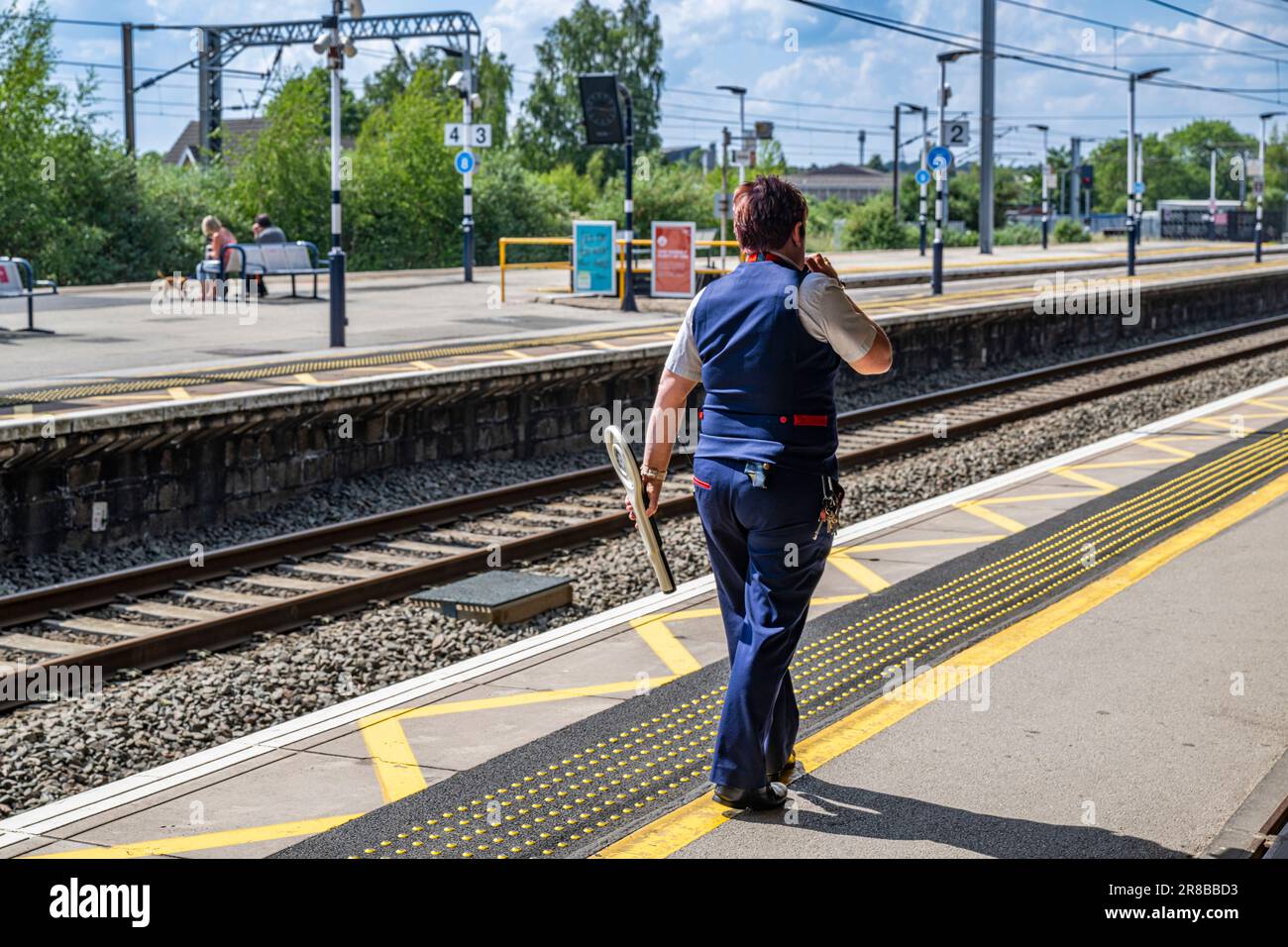 Bahnhof Grantham – Eine Zugführerin oder Wache stand an einem hellen Sommertag auf einem Bahnsteig Stockfoto