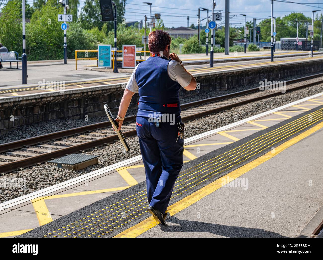 Bahnhof Grantham – Eine Zugführerin oder Wache stand an einem hellen Sommertag auf einem Bahnsteig Stockfoto