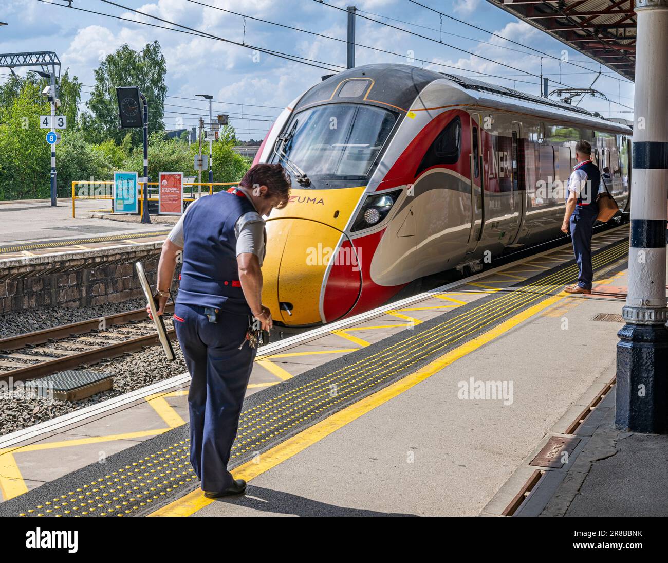 Bahnhof Grantham – Eine Zugführerin oder Wache, die an einem hellen Sommertag auf einem Bahnsteig die Ankunft eines London North Eastern (LNER) Azuma Train beobachtet Stockfoto