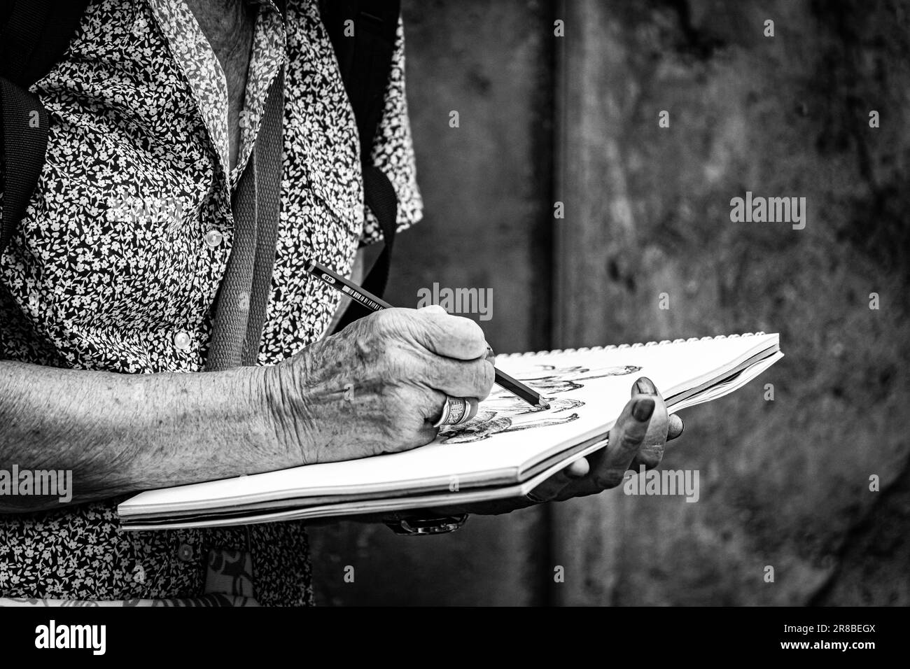 Eine Graustufenaufnahme einer älteren Frau, die mit einem Bleistift zeichnet. Stockfoto