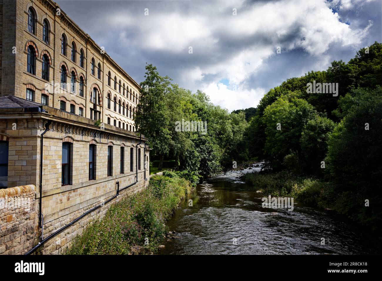 Ein altes Mühlengebäude, das in Wohnungen umgewandelt wurde, neben einem Fluss in einer waldreichen Umgebung, River Irwell, Summerseat, Bury, England Stockfoto