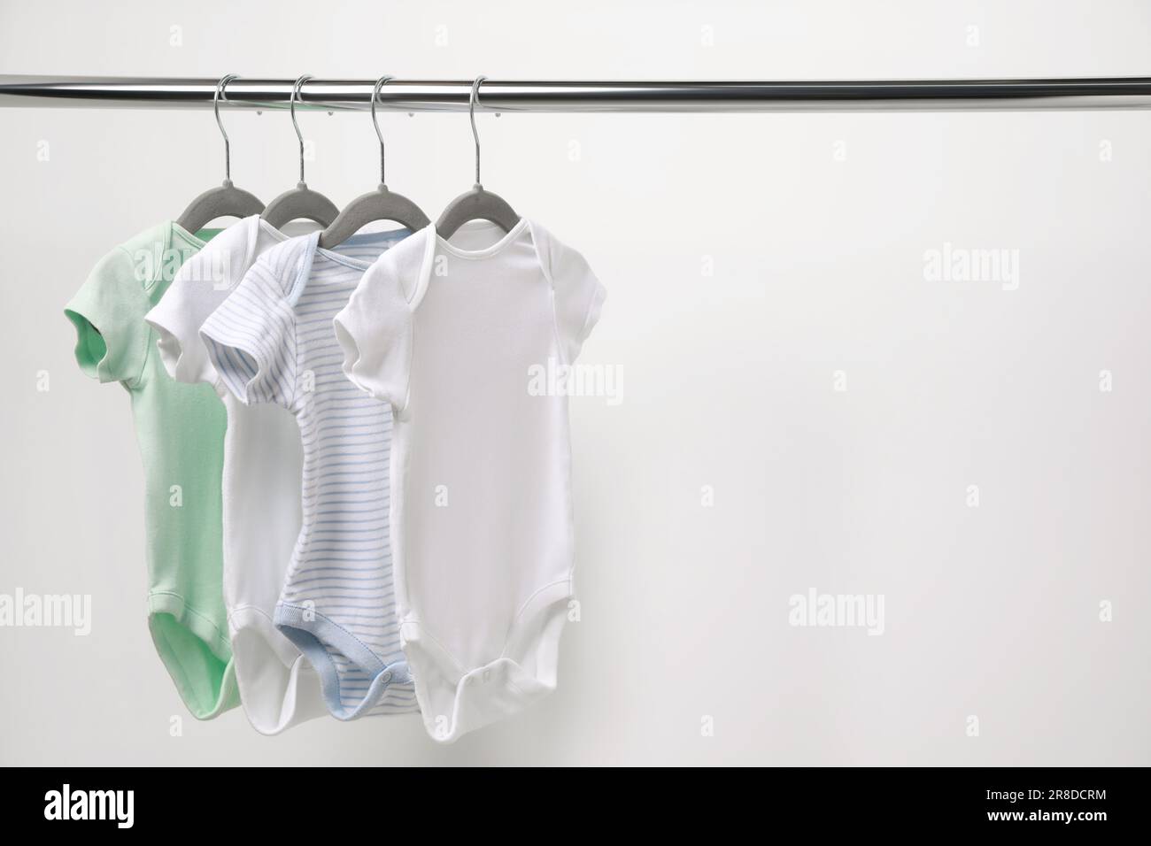 Babykleidung, die an einem Regal in der Nähe der weißen Wand hängt. Platz für Text Stockfoto