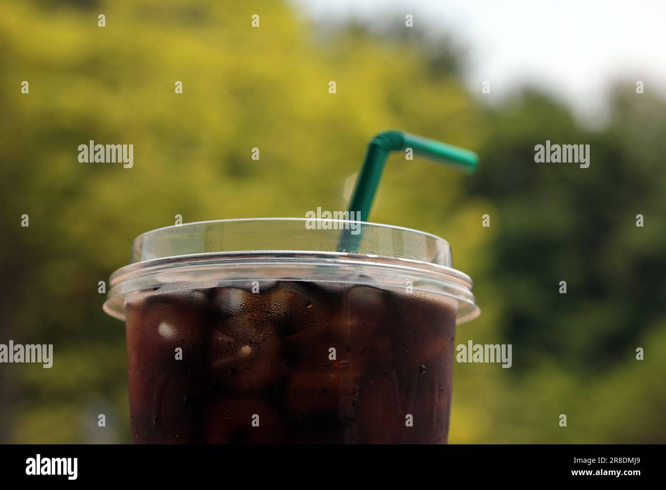 Verschließen Sie den Eiskaffee in einer Plastiktasse. Paket zum Mitnehmen und einfach zu erfrischen. Mit Gartenblick und Bokeh-Hintergrund. Stockfoto
