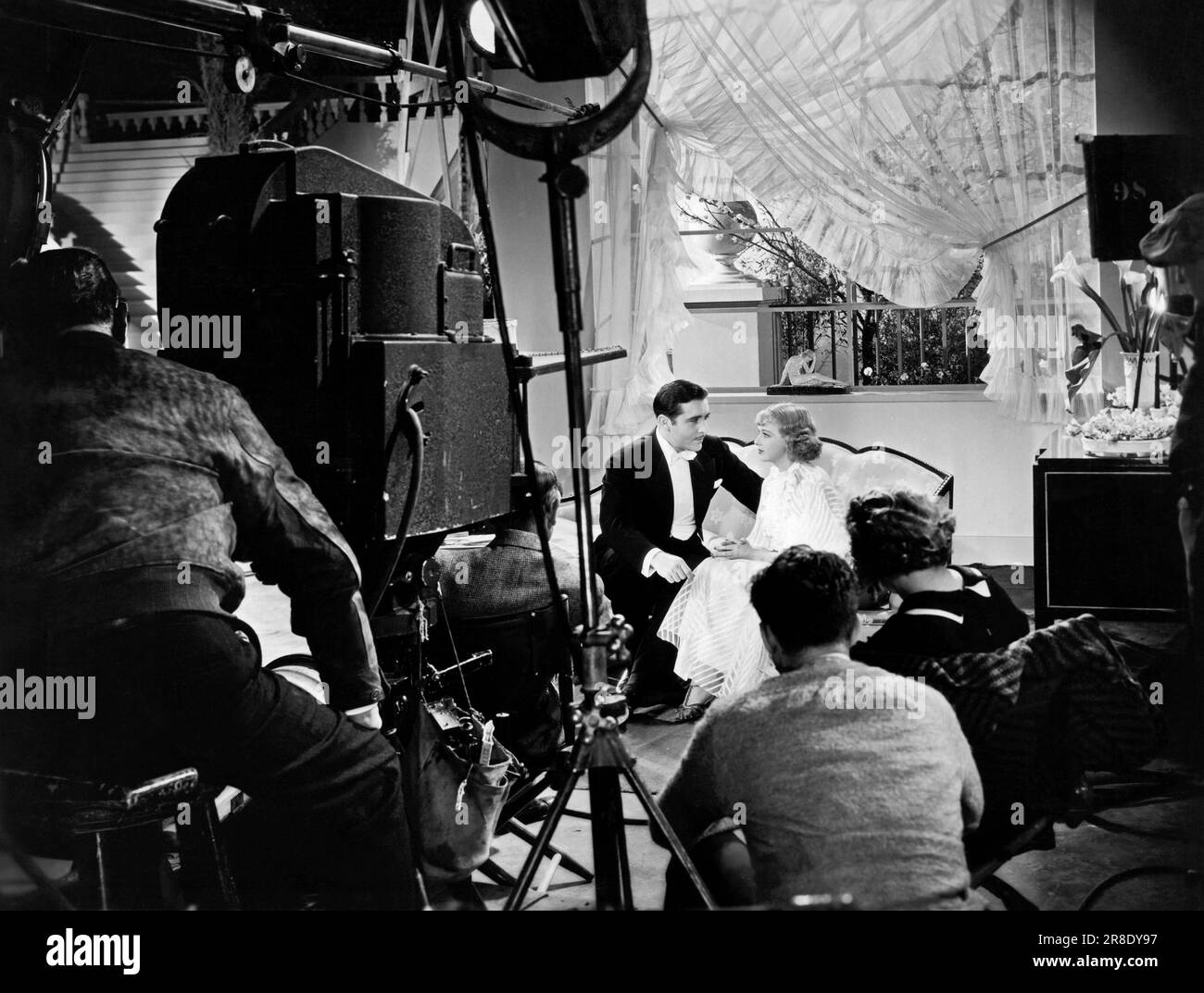 Hollywood, Kalifornien, 1935 Schauspieler John Boles und Dixie Lee versuchen eine Liebesszene im Musical „Redheads on Parade“, während Regisseur, Kamerateam und Drehbuchmädchen zuschauen. Stockfoto
