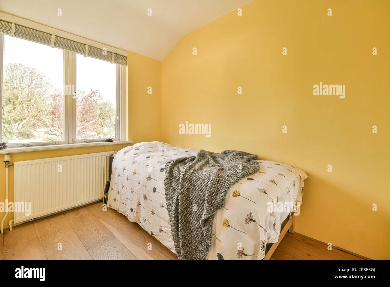 Ein Schlafzimmer mit gelben Wänden und Hartholzfußboden, die das Licht zeigen, das durch die großen Fensterscheiben hereinkommt Stockfoto
