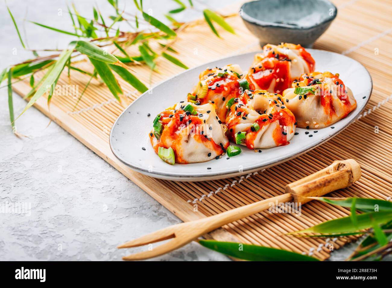 Gedämpfte Teigtaschen Dim Sum mit heißer Sriracha-Sauce und grünen Zwiebeln und Sesamsamen. Stockfoto