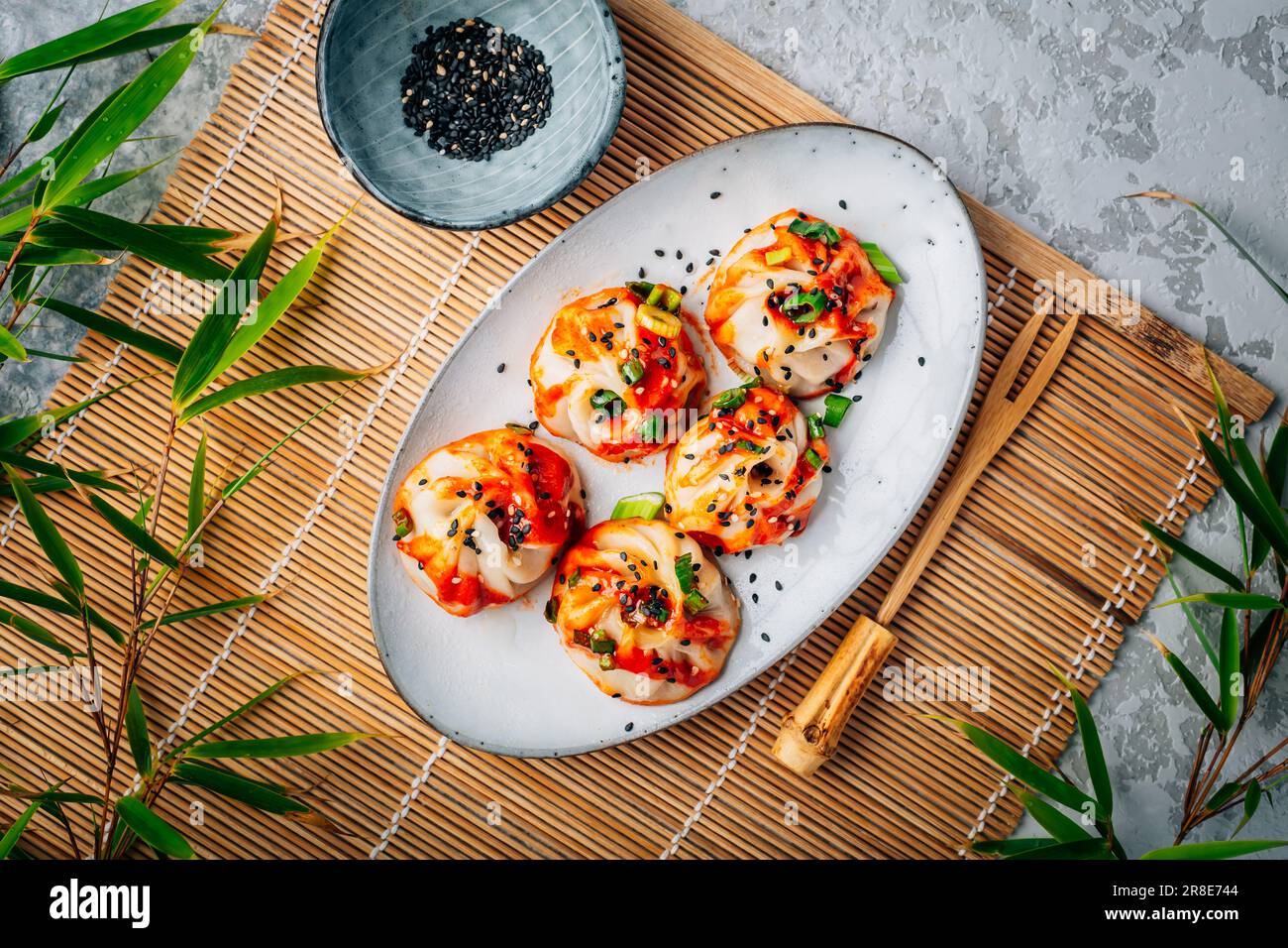 Gedämpfte Teigtaschen Dim Sum mit heißer Sriracha-Sauce und grünen Zwiebeln und Sesamsamen. Stockfoto