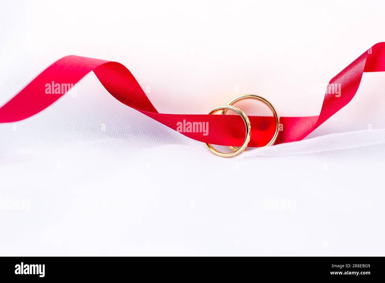 Goldene Eheringe für die Verlobung. Goldene Eheringe mit weißen, rosa Schleifen als Hintergrund. Ringe auf der weißen und roten Rose. Die Eheringe schon Stockfoto