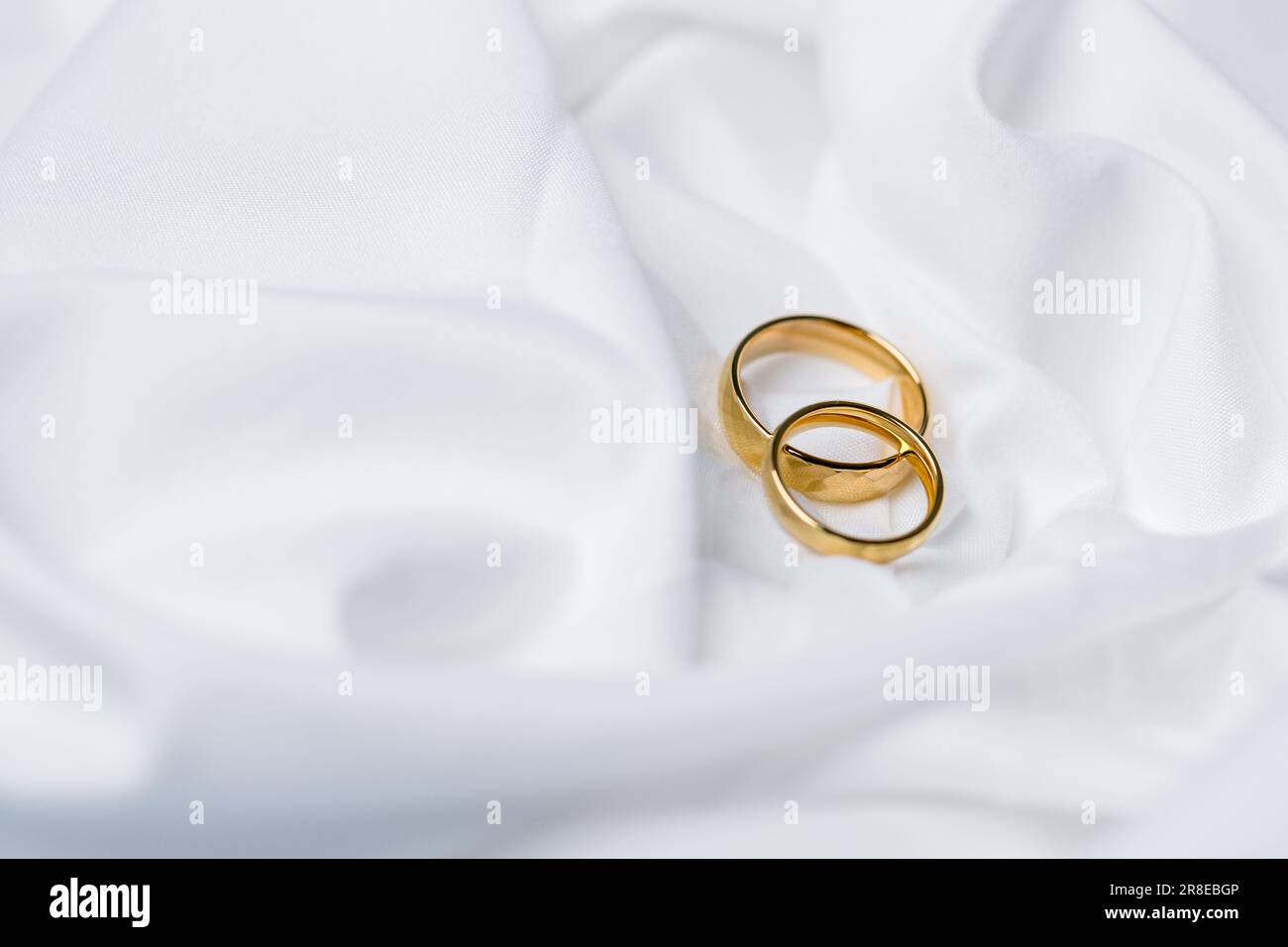 Goldene Eheringe für die Verlobung. Goldene Eheringe mit weißen, rosa Schleifen als Hintergrund. Ringe auf der weißen und roten Rose. Die Eheringe schon Stockfoto