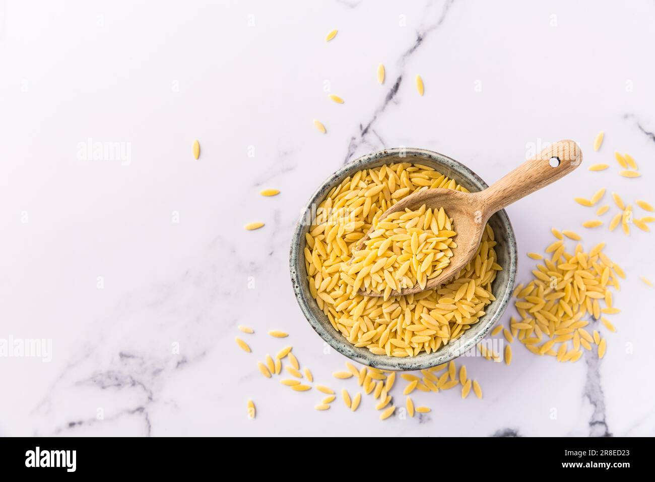 Rohe Orzo-Pasta (Risoni) in Schüssel mit Holzlöffel Stockfoto