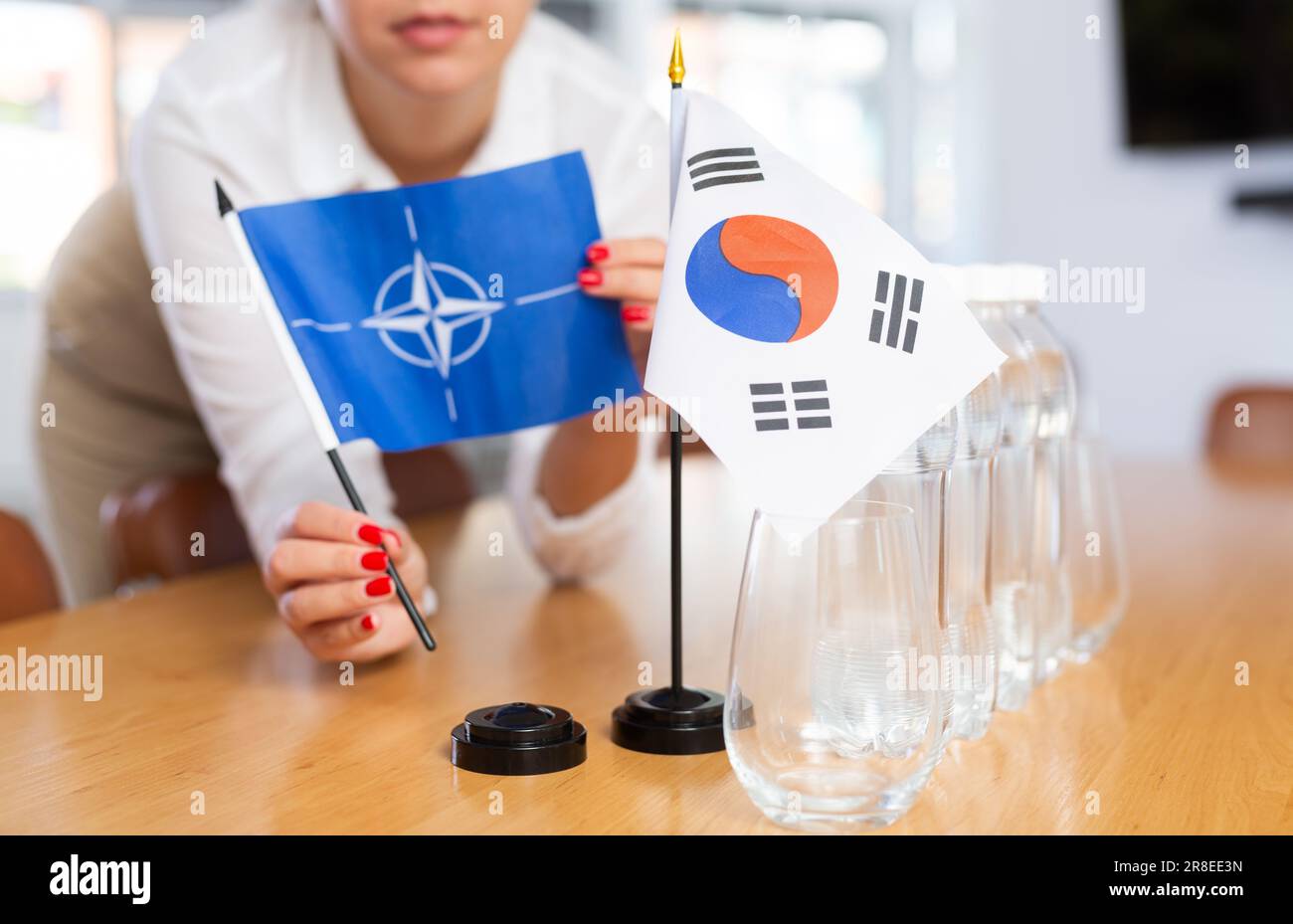 Vorbereitung auf Geschäftsverhandlungen - Frau setzt kleine Flaggen von NATO-Ländern (OTAN) und Südkorea auf den Tisch Stockfoto