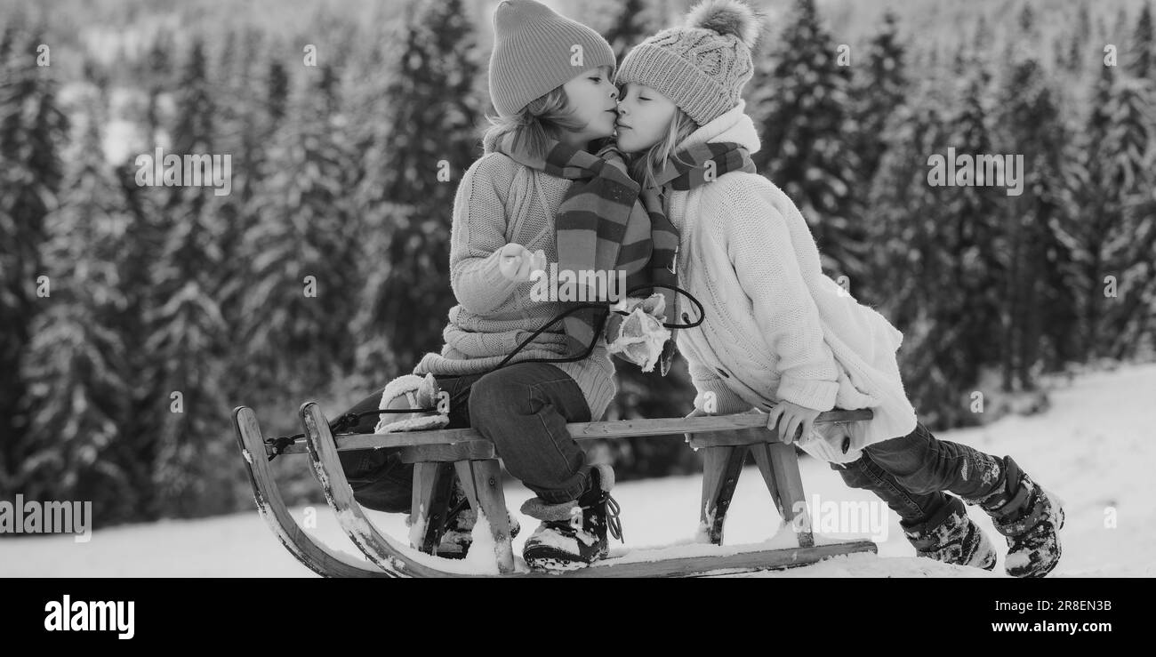 Outdoor Kinder kleiner Junge und Mädchen küssen im Winter im Freien. Glück und Kinder lieben. Kleines Paar auf einem Schlitten küssen. Kumpels geküsst. Stockfoto
