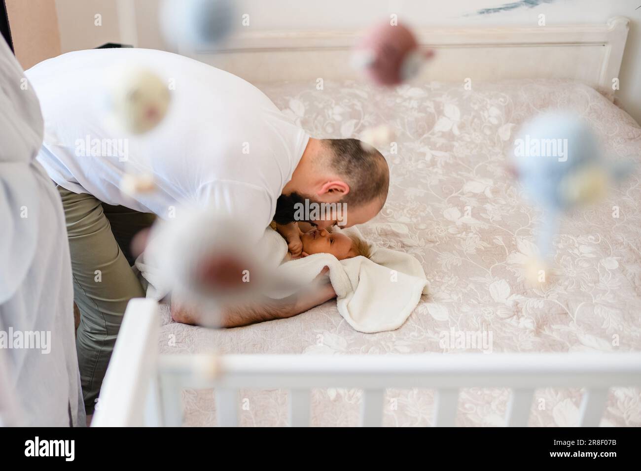 Glücklicher Vater mit neugeborenem Kind im Kinderzimmer, im Bett mit hängendem Spielzeug bei Tageslicht Stockfoto