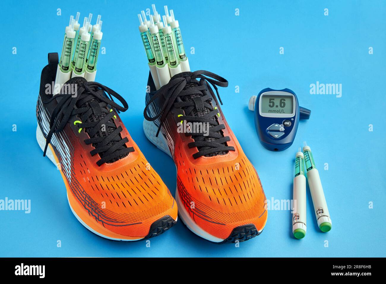 Orangefarbene Turnschuhe mit Insulinspritzen und einem Glukometer auf blauem Hintergrund. Körperliche Aktivität und sportliche Übungen. Lebensstil mit Diabetes Stockfoto