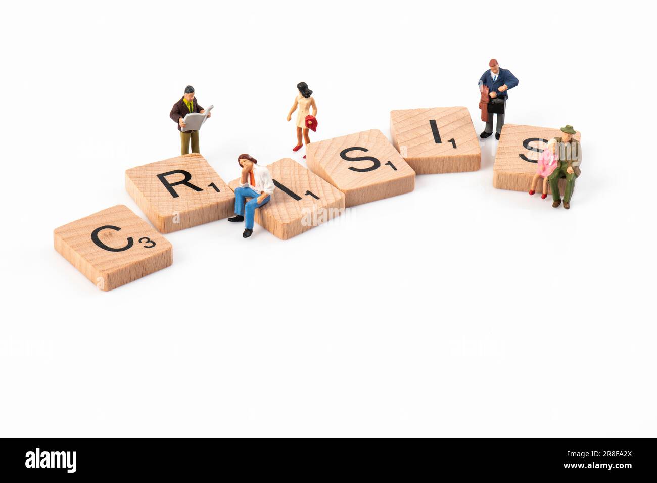 Krise – hölzerne Scrabble-Buchstaben, die „Krise“ buchstabieren, umgeben von kleinen Figuren, die verschiedene Altersgruppen darstellen. Stockfoto