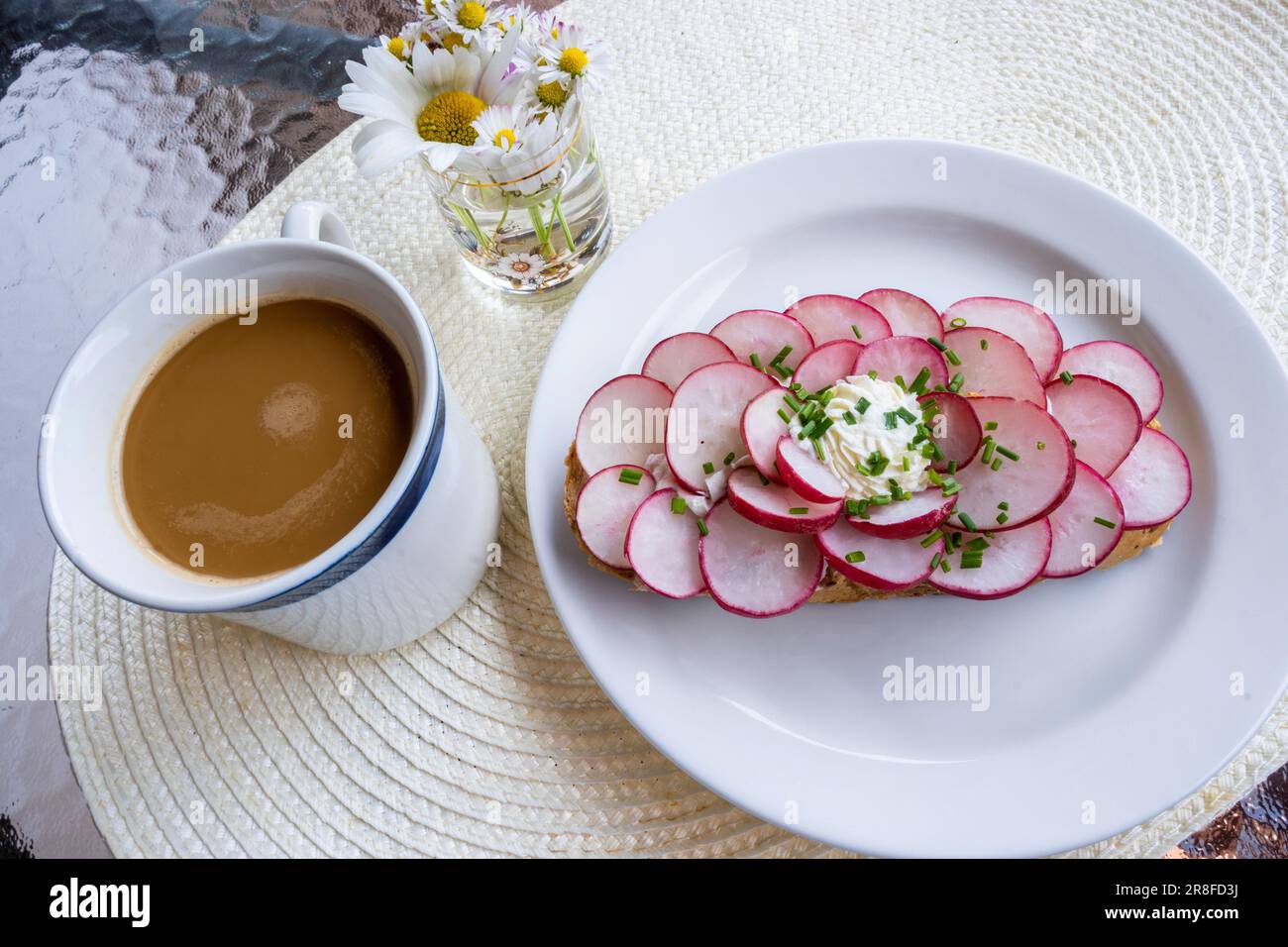Brot garniert mit Radieschen auf weißem Teller, eine Tasse Kaffee, Blumen auf dem Tisch. Stockfoto