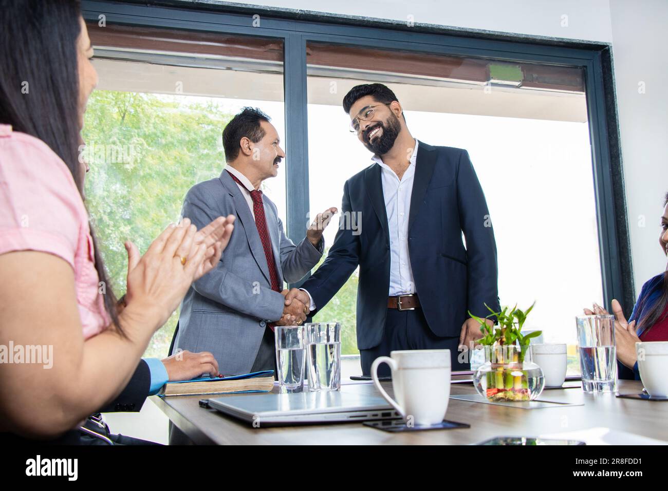 Indische Chefin schüttelt sich die Hand und würdigt Mitarbeiter für gute Arbeit in der Firma, die im Konferenzraum steht. Stockfoto