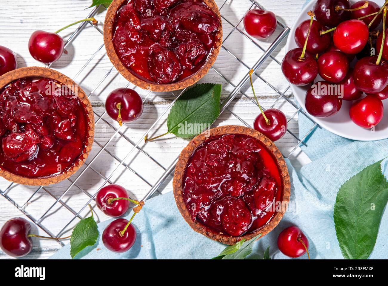 Kirschdesserttörtchen. Mini-Törtchen mit Sahne- und Kirschfüllung, traditioneller Sommerkuchen, mit frischen Kirschen auf weißem Holzhintergrund Stockfoto