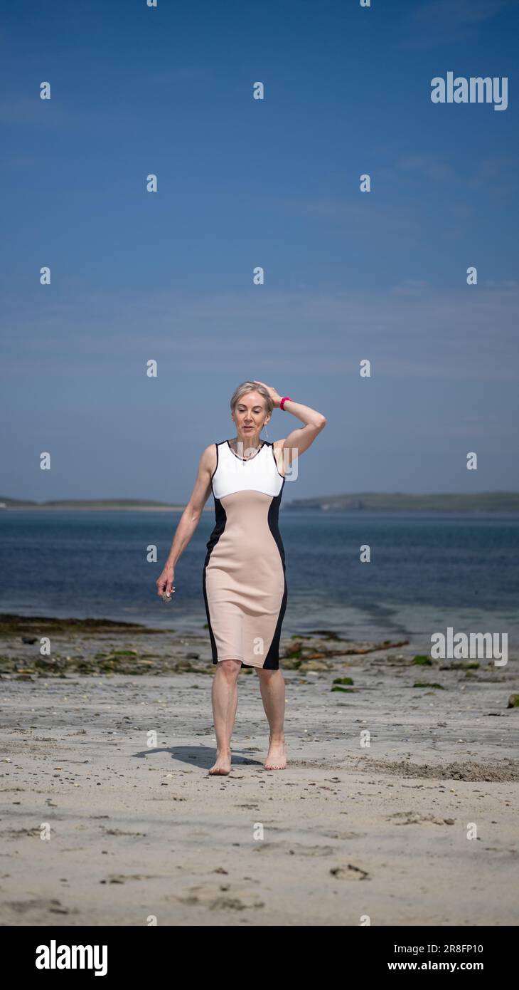 Frau in einem eleganten Kleid, die barfuß an einem Sandstrand auf den Orkney Isles, Schottland, Großbritannien, spaziert Stockfoto