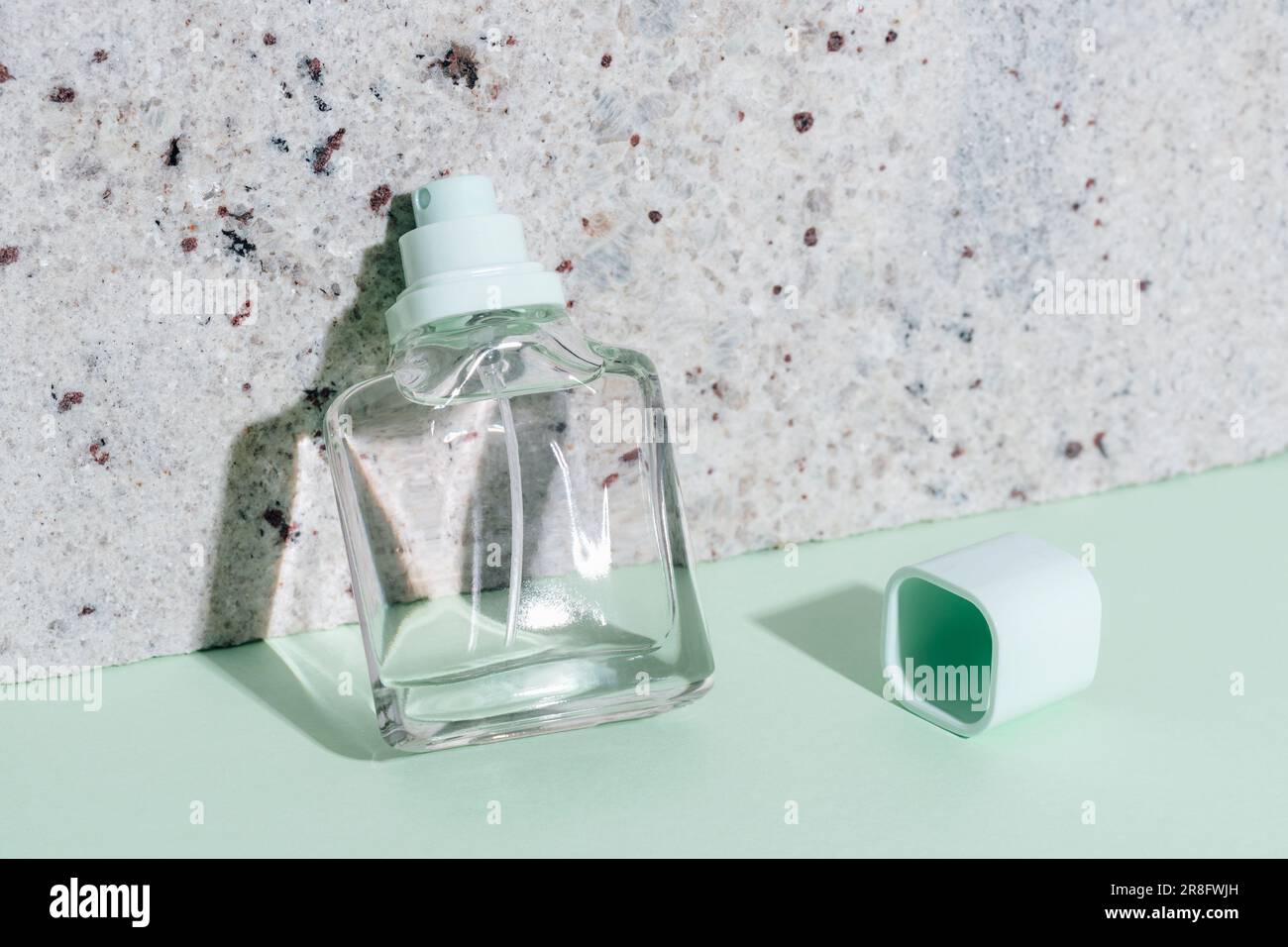 Parfümflasche auf grünem Tisch mit harten Schatten und Marmorsteinhintergrund. Modell. Stockfoto