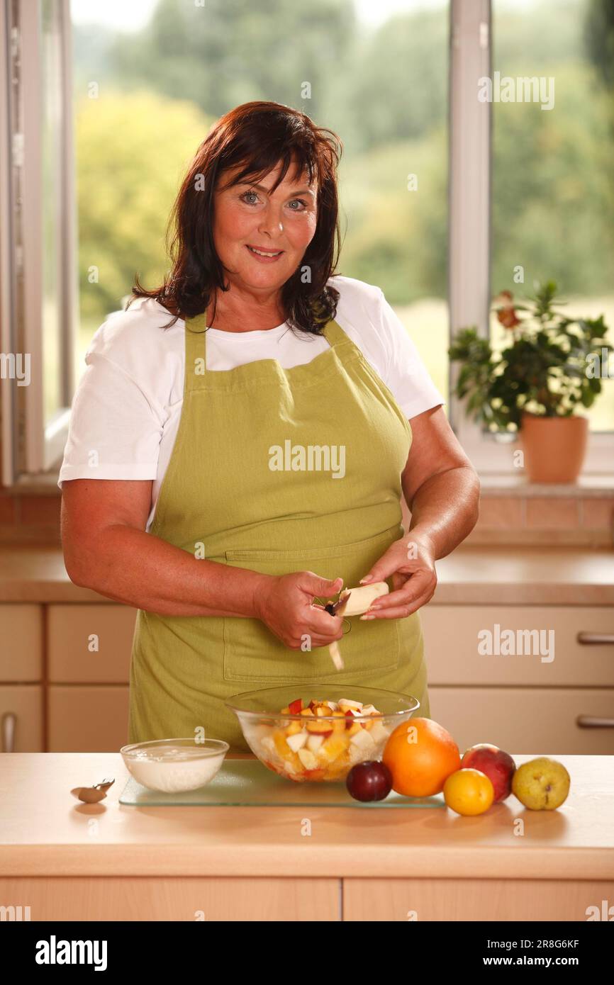 Frau bereitet Obstsalat zu, bereitet ihn vor, schält, schält, schält, Joghurt, klein geschnitten, Messer Stockfoto