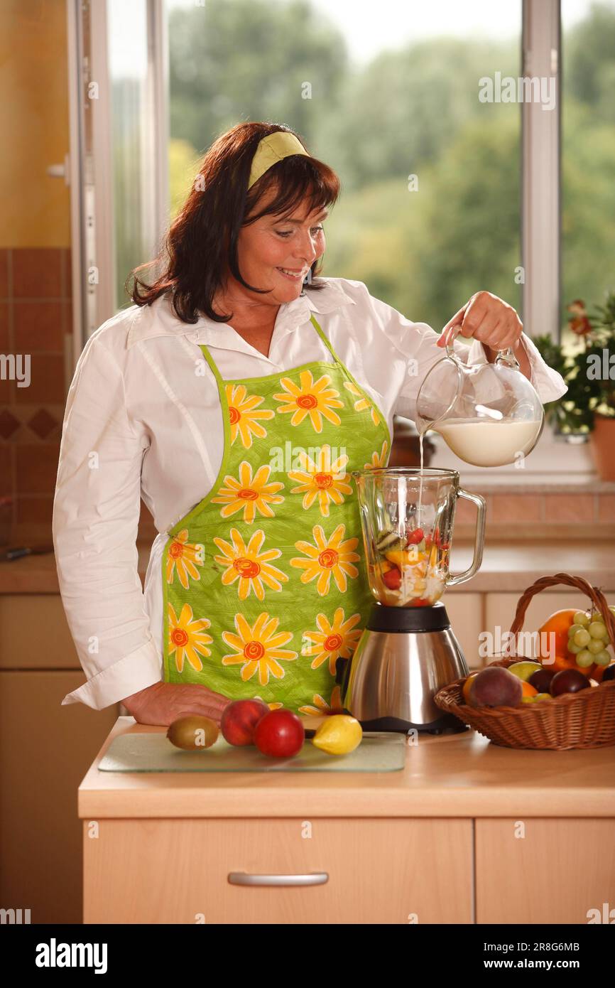 Frau gießt Milch zu Früchten in den Mixer, bereitet sie vor, stellt sie auf, mischt, gießt sie, Gießen, eingießen, hinzufügen, mischen, hinzufügen, Obstkorb, Korb, Haarband Stockfoto