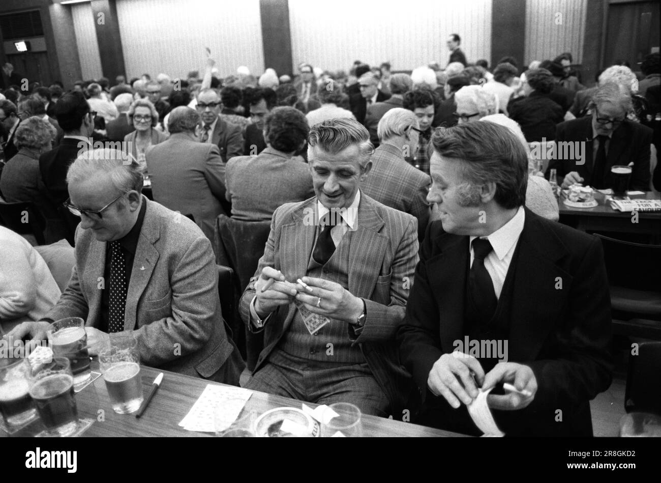 Männer spielen Bingo UK 1980er. Coventry Working Mens Club, Samstagabend Bingo Abendunterhaltung. Sie sehen schick aus, zwei Männer, die sich unterhalten und rauchen. Coventry, England, etwa 1981. Stockfoto