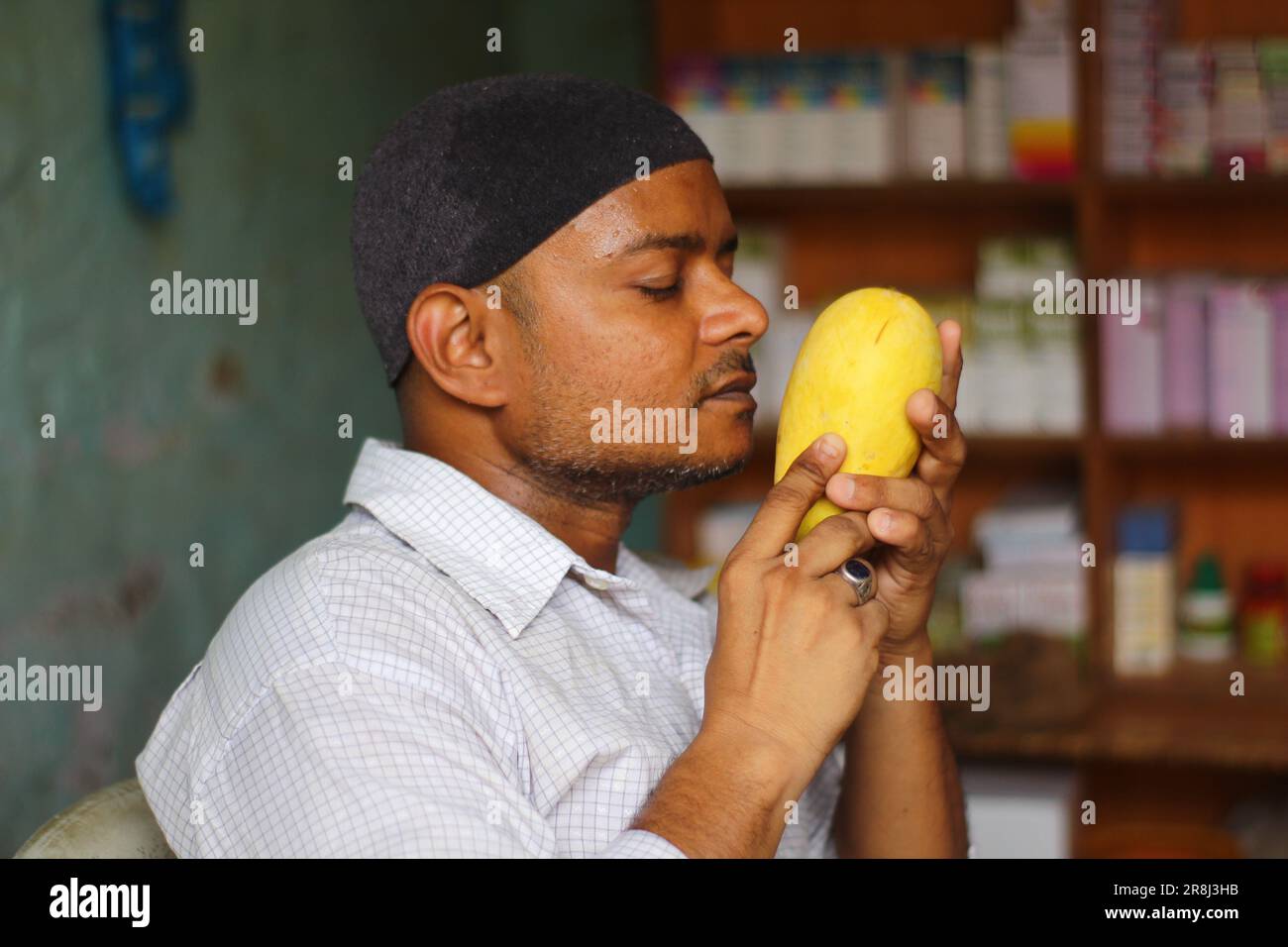 Ein asiatischer Schwarzer, der eine Mango in der Hand hält und die Pose der riechen Mango mit Mütze und Ring im Finger gibt Stockfoto