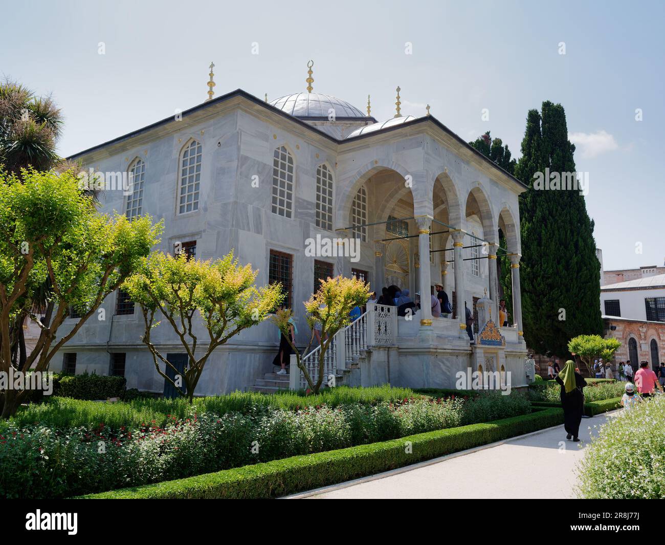 Außenansicht des Topkapi Palace Musuem Komplexes mit Gärten. Bezirk Fatih, Istanbul, Türkei. Die muslimische Dame geht an einem eleganten Gebäude mit Säulengang vorbei Stockfoto