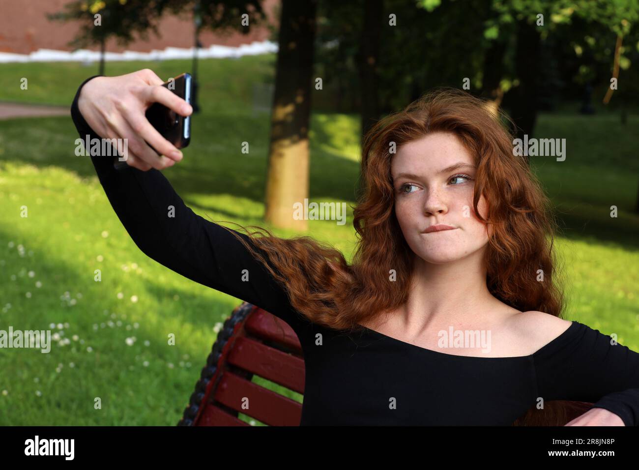 Attraktives Mädchen mit langen roten Haaren, das Selfie mit einer Smartphone-Kamera im Sommerpark macht. Junges Model, natürliche weibliche Schönheit Stockfoto