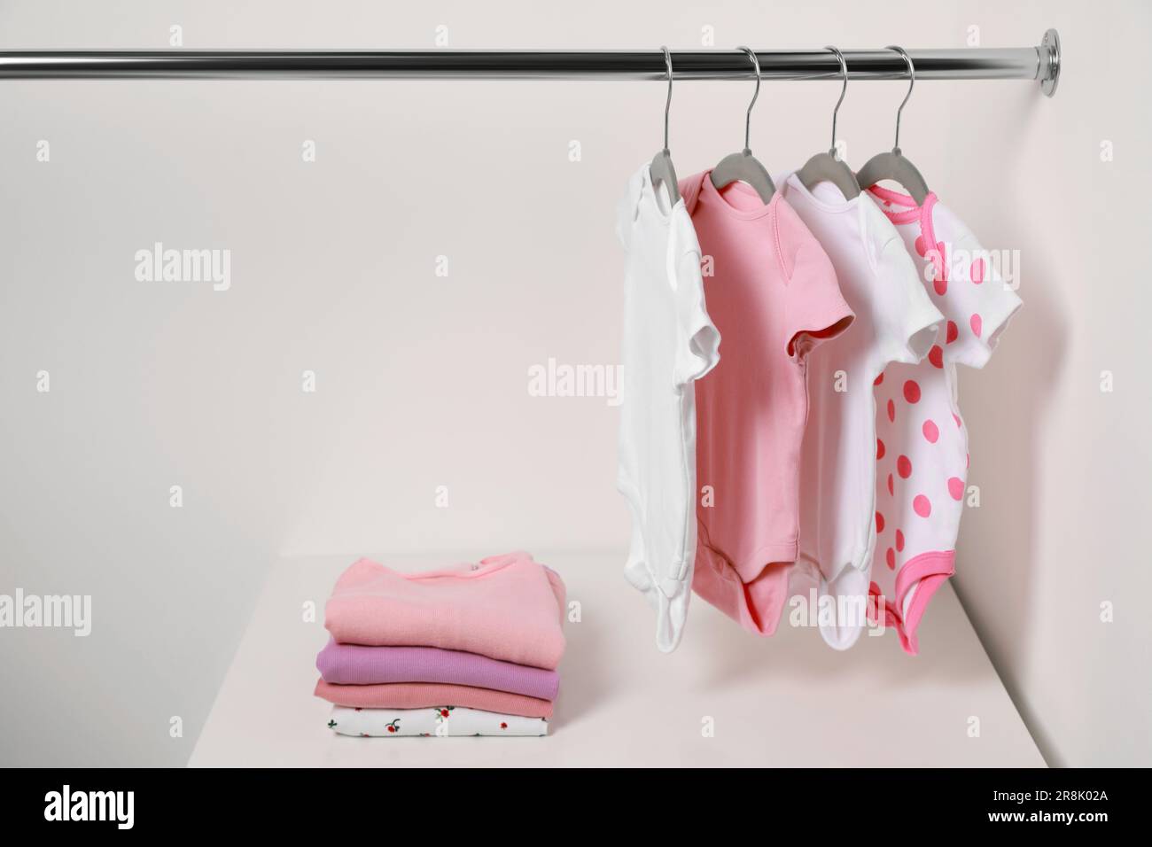 Kleiderbügel mit Babybekleidung und Kleiderstapel in der Nähe der weißen Wand. Platz für Text Stockfoto
