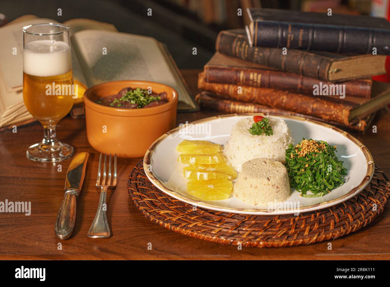 Wunderschönes Gericht mit Feijoada und Bier. Im Hintergrund alte Bücher Stockfoto