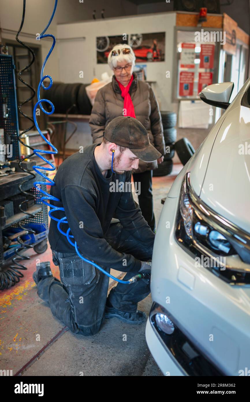 Mechaniker in der Garage wechselt Reifen am Auto und spricht mit einer Klientin Stockfoto