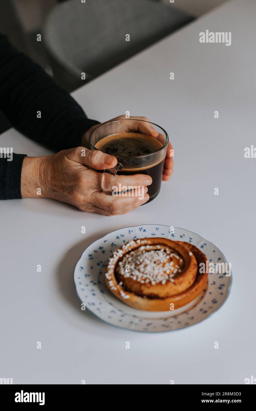 Hände halten die Kaffeetasse mit Zimtrollen auf dem Tisch Stockfoto