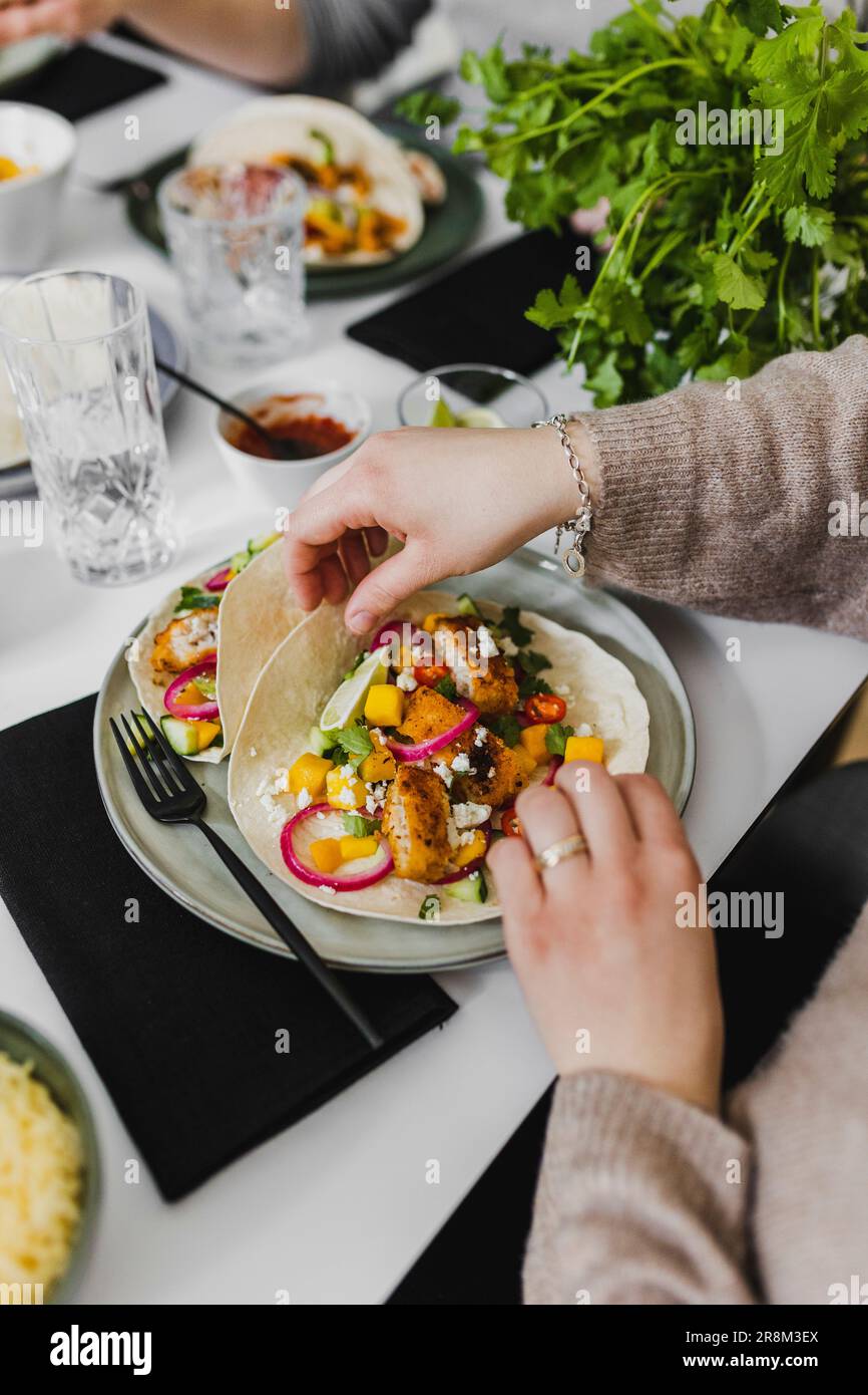 Person, die mexikanische Tortilla mit verschiedenen Belägen umhüllt Stockfoto