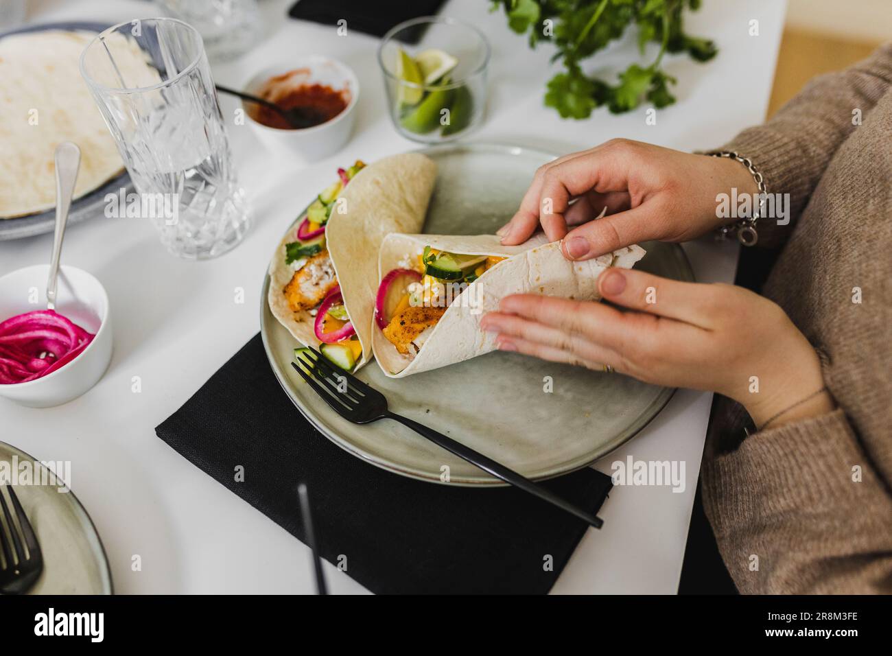 Person, die mexikanische Tortilla mit verschiedenen Belägen umhüllt Stockfoto