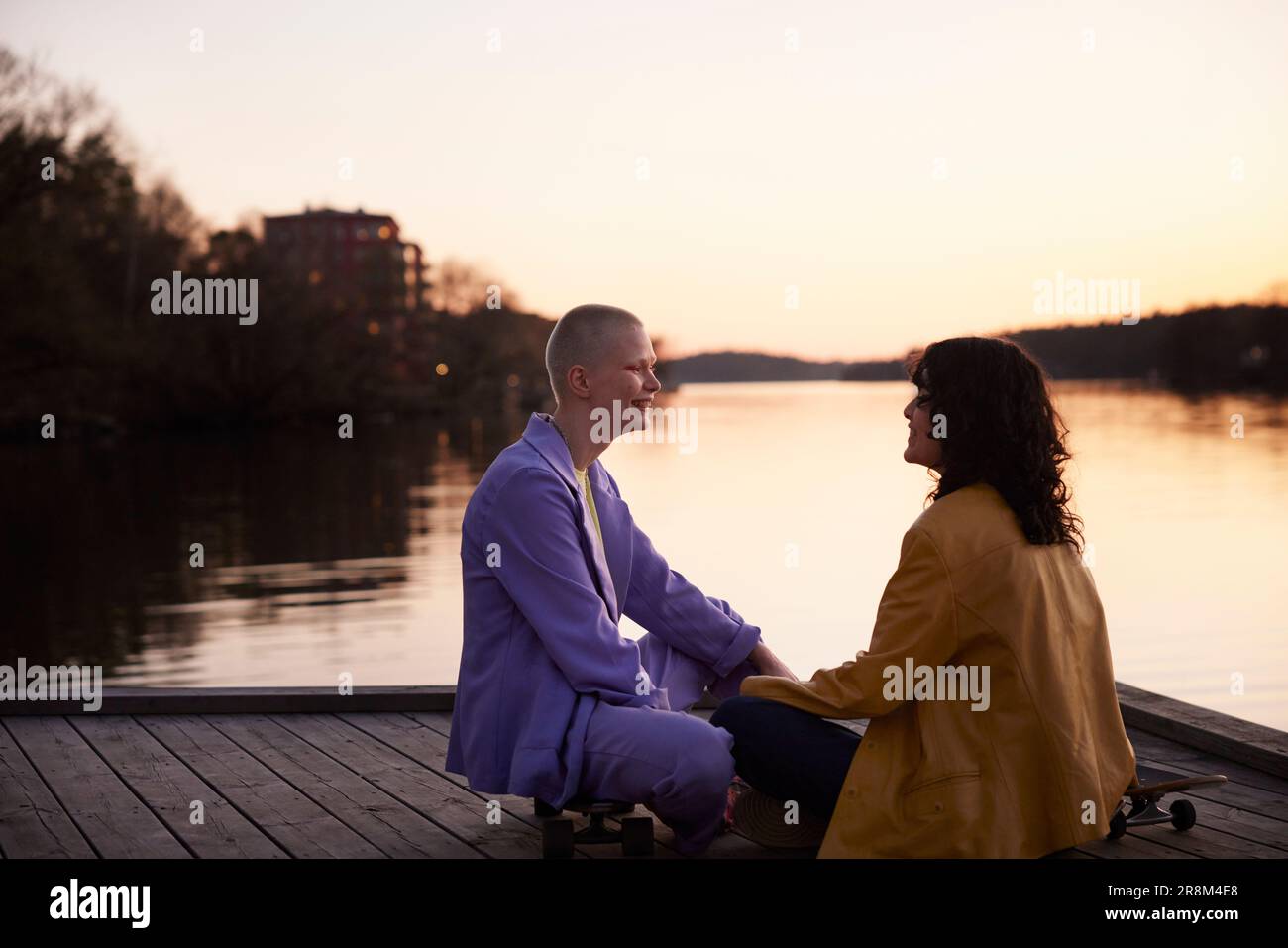 Ein junges weibliches schwules Paar sitzt und schaut sich am Fluss an Stockfoto