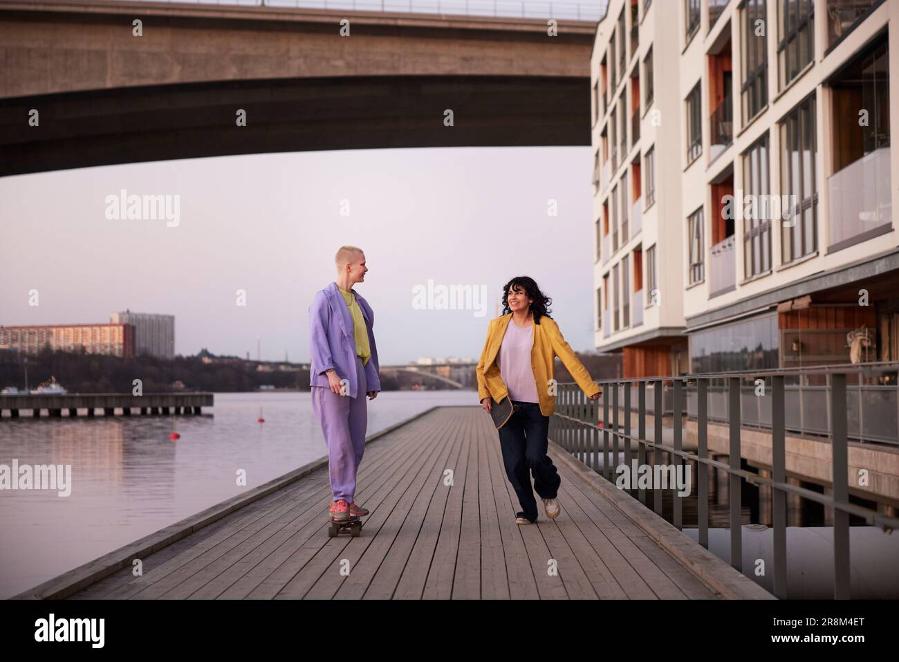 Weibliche Freunde oder schwule Paare auf der Promenade, eine Frau läuft, während andere Skateboarden Stockfoto